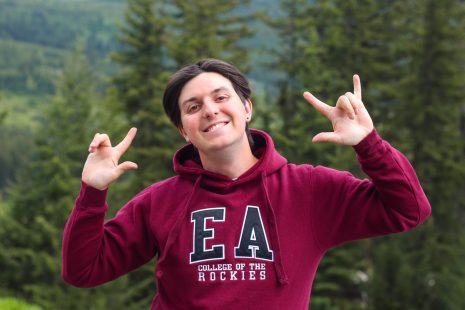 Image shows man in a COTR EA hoodie outdoors sharing a message using ASL.