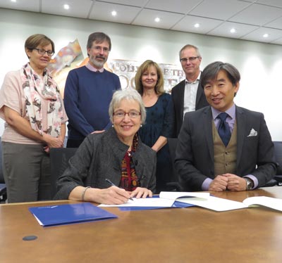 Image of Dr. Catherine Mateer from UVIC signing agreement as College VP Stan Chung and other Executive members look on.