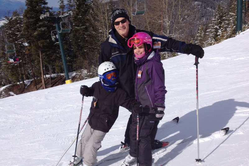 An image of a man and two children posing on a ski hill.