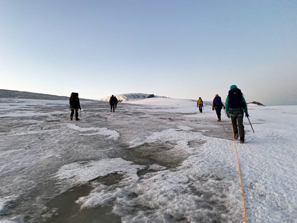 Image shows individuals hiking on a glacier.