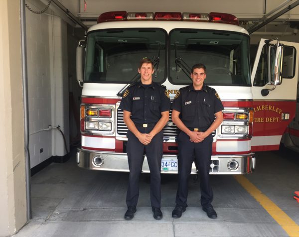 Image of two young men in firefighter uniforms standing in front of a Kimberely Fire Dept. fire truck.