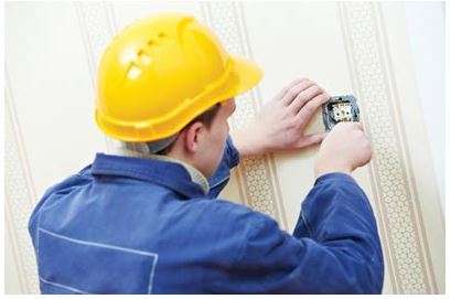 Image of male in hard hat working on an electrical outlet on a wall.