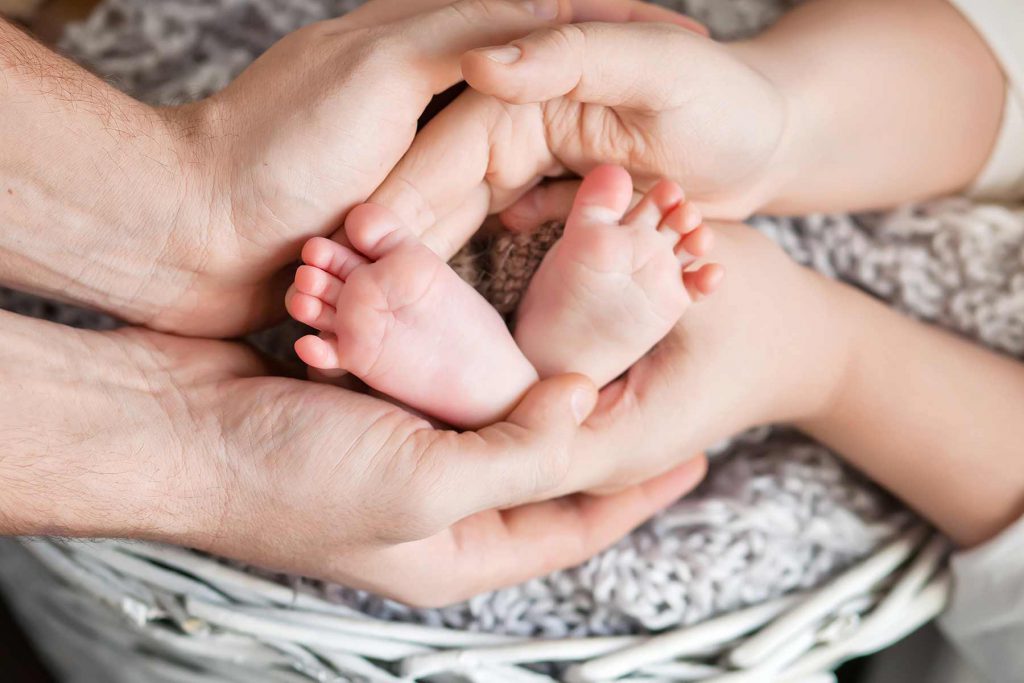 Two sets of hands cradling a newborn baby's feet.