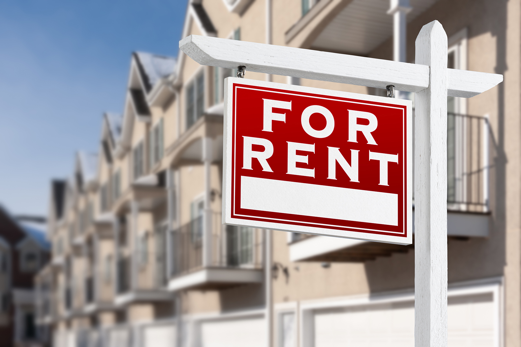 For Rent Real Estate Sign In Front of a Row of Apartment Condominiums Balconies and Garage Doors.