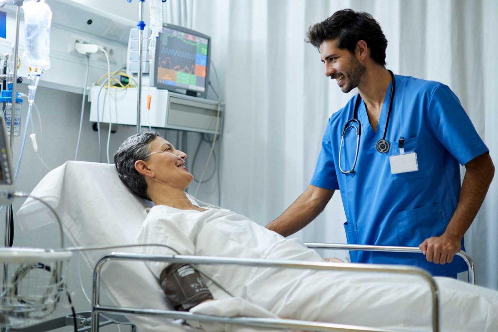 An image of a male nurse speaking with a patient in a hospital bed.