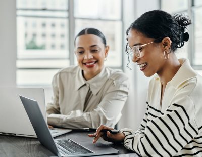 Business women, laptop and and happy team in office for web design, collaboration and training. Planning, digital marketing and coaching by woman leader menor help, explain and support creative goal