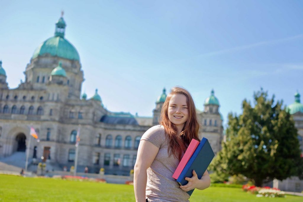 An image of a student with textbooks standing outside the Parliament buildings.