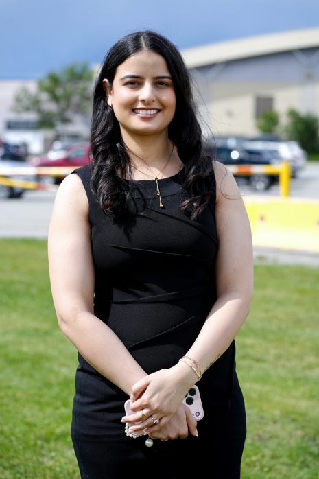Image shows woman in black dress, with long dark hair, smiling at the camera.