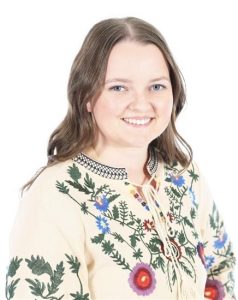 Image shows young woman in a colourful top, smiling at the camera.
