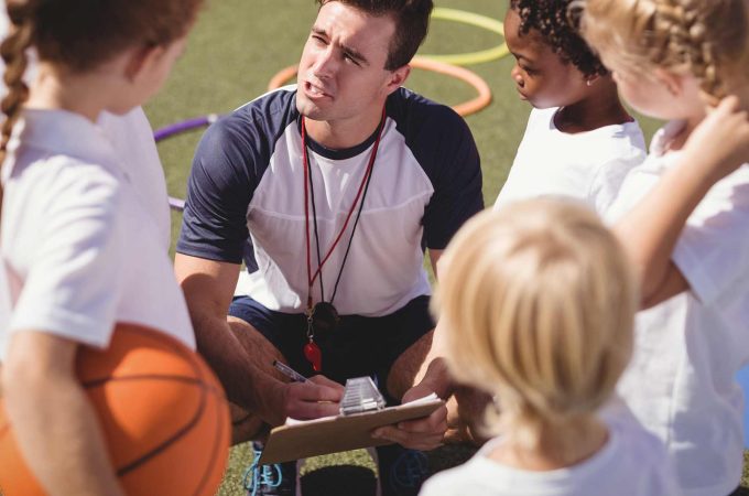 Coach with group of young kids. One girl is holding a basketball.